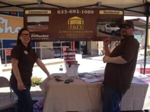 Two F&J’s Garage Door Service employees, a woman and a man, stand behind a table at a community event.